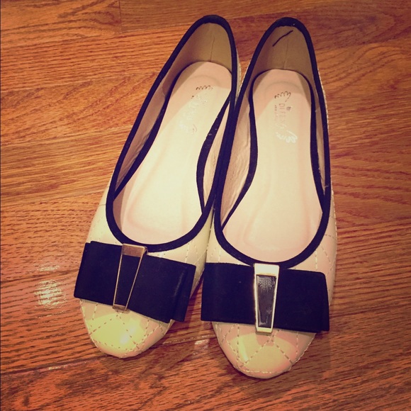Cream colored flats with black bow on top.