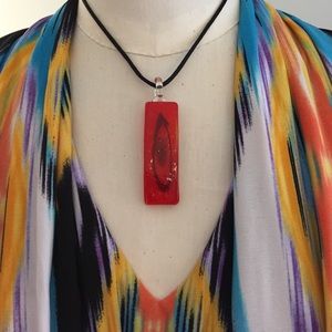 Rectangular red glass enhancer on a black cord.
