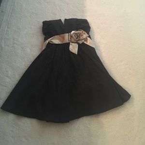 Short black dress with gold ribbon and flower.