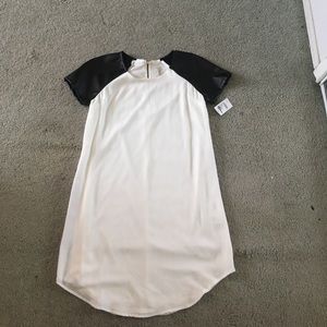 White shift dress with black leather sleeves.