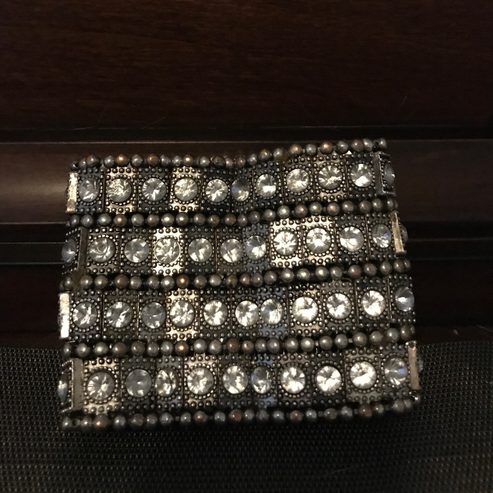 A thick dark metal bracelet with clear stones.