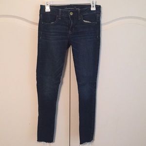 Blue jeans with frayed ankle hems.