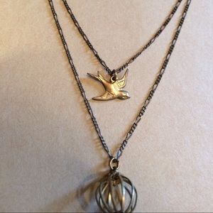 Layered necklace with bird and cage design.